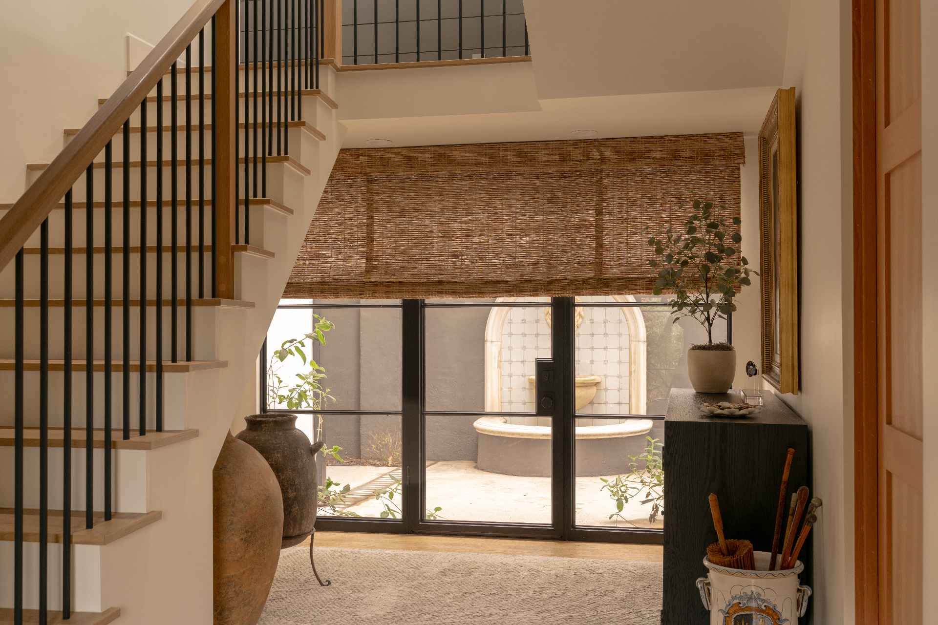 Natural woven shade in a sunlit entryway with staircase and courtyard view