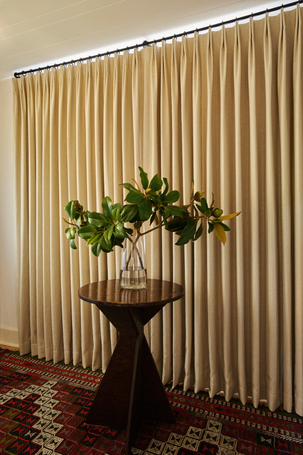 Pleated floor-to-ceiling drapery behind a sculpted side table